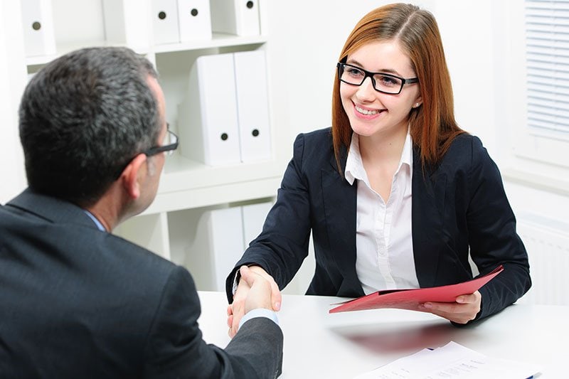 woman shaking hands with male sitting at desk